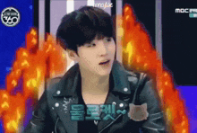 a young man in a black leather jacket is standing in front of a fire .