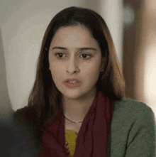 a woman wearing a scarf and a green sweater is looking at the camera with a serious look on her face .