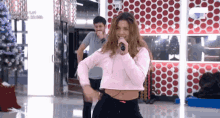 a woman in a pink crop top singing into a microphone while a man watches