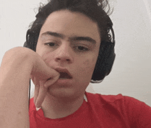 a young man wearing headphones and a red shirt is biting his nails