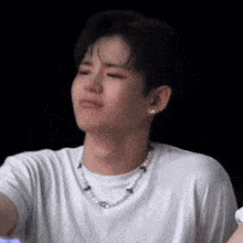 a young man wearing a white shirt and a pearl necklace is making a sad face .