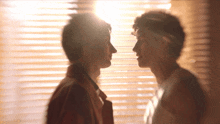 two men are looking at each other in front of blinds