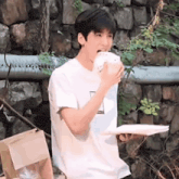 a young man in a white t-shirt is eating a hamburger while holding a plate .