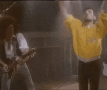 a man in a yellow sweater is holding a microphone in his hand .