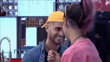 a man wearing a yellow hat and a woman wearing a pink shirt are holding hands .