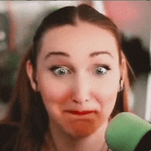 a close up of a woman making a funny face while holding a green microphone .