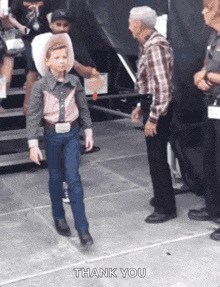 a young boy in a cowboy outfit is walking in front of an older man and saying thank you .