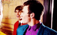 a man wearing a purple shirt and a blue jacket is standing next to two other men .