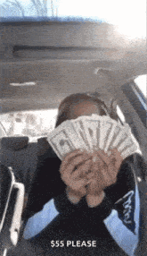 a woman is sitting in the back seat of a car holding a fan of money .