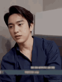 a young man in a blue shirt is sitting at a table and looking at something .