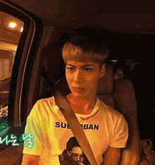 a young man wearing a t-shirt that says suburban is sitting in a car