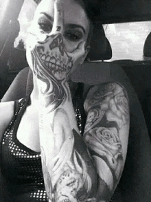 a woman with a skeleton tattoo on her face is sitting in a car covering her face with her hand .