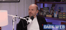 a man sitting in front of a microphone with the words dark web on the bottom right