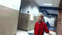 a boy in a red shirt walks down a hallway