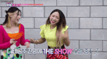 two women are standing in front of a brick wall with the show written on the bottom right