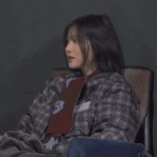 a woman is sitting in a chair wearing a plaid shirt and a red shirt .