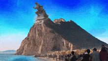 a group of people standing on a beach in front of a mountain with a statue on top of it