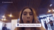 a woman is making a funny face in front of a map that says ana clara nos estudios globo