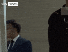 a man in a suit and tie stands next to a woman in a yellow vest that says sky news