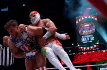 two wrestlers in a ring with a sign that says saturday july 12