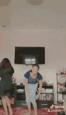 two women are dancing in a living room in front of a tv .