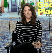 a woman in a black and white striped shirt is sitting in front of a screen that says the good place