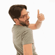 a man wearing glasses and a grey shirt is standing with his arms crossed