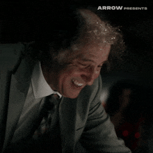 a man in a suit and tie is smiling in front of an arrow presents sign