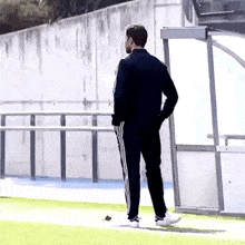 a man in a black jacket and white pants is standing on a soccer field