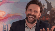 a man with a beard is laughing with his eyes closed in front of a castle .