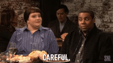 a man and a woman are sitting at a table with a plate of food and a sign that says careful