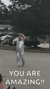 a man in a white bodysuit is dancing on a street .