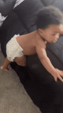 a baby wearing a diaper is crawling on a black couch