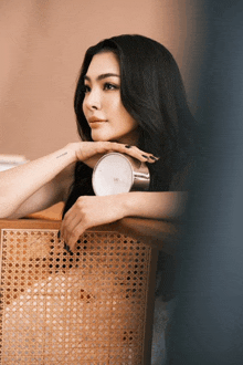 a woman leaning on a wicker chair holding a silver clock