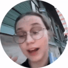 a woman wearing glasses is standing in front of a building and making a funny face .