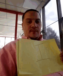 a man in a pink shirt is holding a piece of paper with the letter i written on it