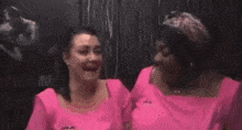two women in pink shirts are laughing and hugging