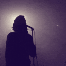 a silhouette of a person singing into a microphone in a dark room