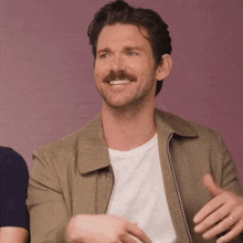 a man with a mustache wearing a green jacket and a white shirt is smiling