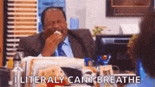 a man in a suit is sitting at a desk eating a sandwich .
