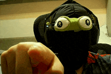 a person wearing headphones and a mask with frog eyes pointing