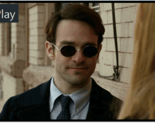 a man wearing sunglasses and a suit stands in front of a sign that says " play "