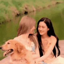 two women are sitting on a dock holding a dog and smiling .