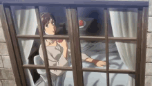 a woman is sitting on a bed looking out of a window eating an apple .