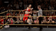 two women are wrestling in a ring with a referee in front of a crowd that is watching