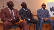 three men in suits sit in chairs in front of a sign that says " no smoking "