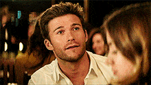 a man with a beard and a white shirt is talking to a woman in a crowded room .