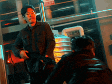 a man in a black jacket holds a gun in front of a sign that says a2