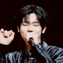 a young man in a leather jacket is holding a microphone in his hand .