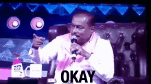 a man is holding a microphone and the word okay is on the screen behind him